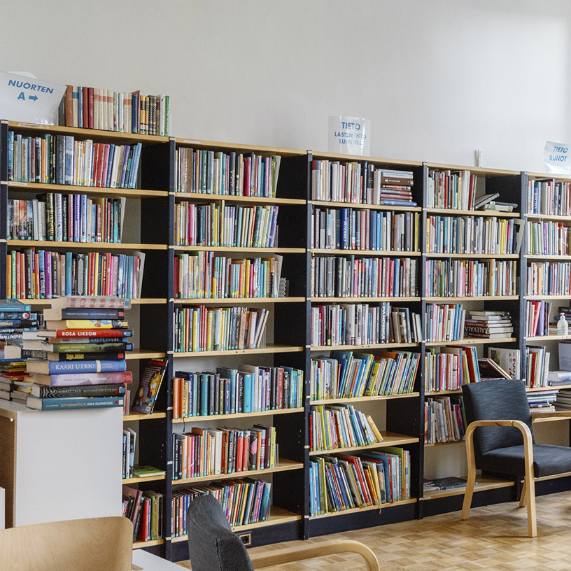 Valkoista seinää vasten kirjahylly, jossa paljon erivärisiä kirjoja.